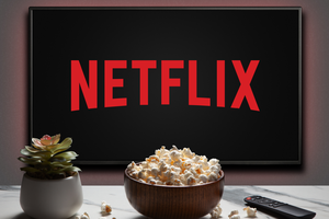 Telewizor wyświetlający logo Netflix, obok miska popcornu i pilot. Roślina doniczkowa w tle.