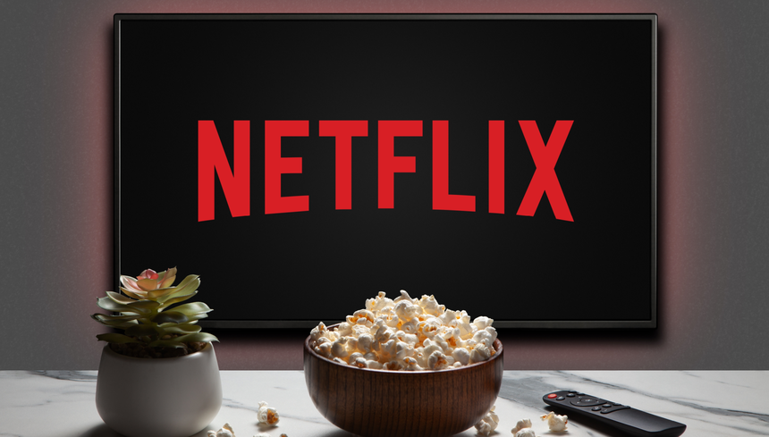 Telewizor wyświetlający logo Netflix, obok miska popcornu i pilot. Roślina doniczkowa w tle.