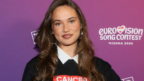 Dziewczyna w czarnej koszulce, na tle fioletowym, uśmiechnięta.