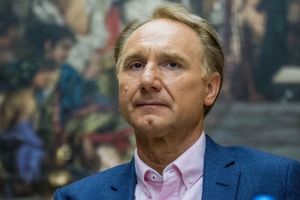 Mężczyzna w jasnej koszuli i granatowym żakiecie, poważnie spogląda w stronę kamery.
