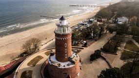 Latarnię morską otacza plaża, morze i promenada z zabudową nadmorską.