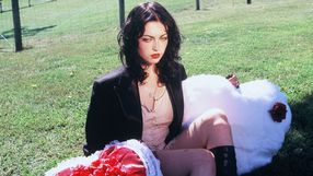 Kobieta w czarnej marynarce siedzi na trawie, trzymając różowy element dekoracyjny.