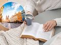 Kobieta w białym swetrze trzyma filiżankę kawy obok otwartej książki na szarym stole.