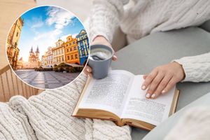 Kobieta w białym swetrze trzyma filiżankę kawy obok otwartej książki na szarym stole.