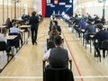 Sala egzaminacyjna z uczniami przy biurkach. Na pierwszym planie uczniowie w garniturach.