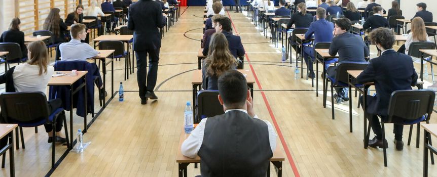 Sala egzaminacyjna z uczniami przy biurkach. Na pierwszym planie uczniowie w garniturach.