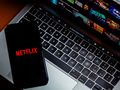 Smartfon z logo Netflix na klawiaturze laptopa, w tle zdjęcia programów telewizyjnych.