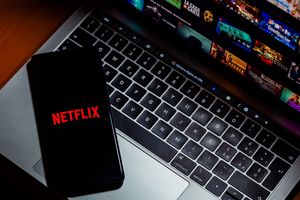 Smartfon z logo Netflix na klawiaturze laptopa, w tle zdjęcia programów telewizyjnych.