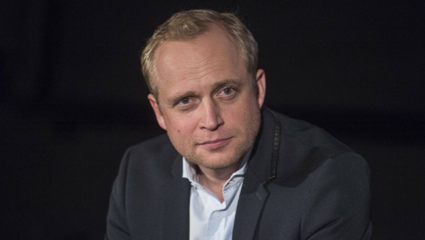 Na zdjęciu mężczyzna w granatowej marynarce, z krótkimi blond włosami, patrzy w obiektyw.