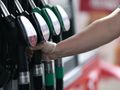 Osoba w rękawiczce trzyma wąż dystrybutora paliwa na stacji benzynowej.