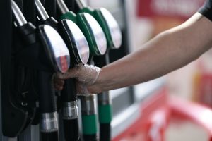 Osoba w rękawiczce trzyma wąż dystrybutora paliwa na stacji benzynowej.