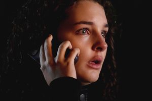 Kobieta z ciemnymi, kręconymi włosami trzyma telefon, wygląda na zaniepokojoną i zdenerwowaną.