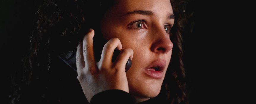 Kobieta z ciemnymi, kręconymi włosami trzyma telefon, wygląda na zaniepokojoną i zdenerwowaną.