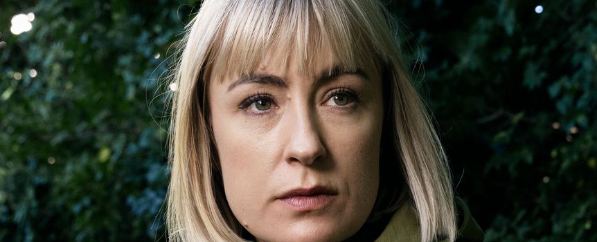 Na zdjęciu widoczna jest kobieta z blond włosami, ubrana w zieloną kurtkę, w tle zieleń.