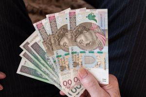 Zdjęcie przedstawia rękę trzymającą kilka polskich banknotów o różnych nominałach.