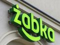Zielony neonowy szyld z napisem „żabka” na jasnej ścianie budynku.