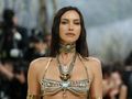 Irina Shayk w bogato zdobionej biżuterii, patrzy pewnie w obiektyw, otoczona przez paparazzi.