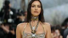 Irina Shayk w bogato zdobionej biżuterii, patrzy pewnie w obiektyw, otoczona przez paparazzi.