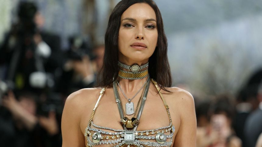 Irina Shayk w bogato zdobionej biżuterii, patrzy pewnie w obiektyw, otoczona przez paparazzi.