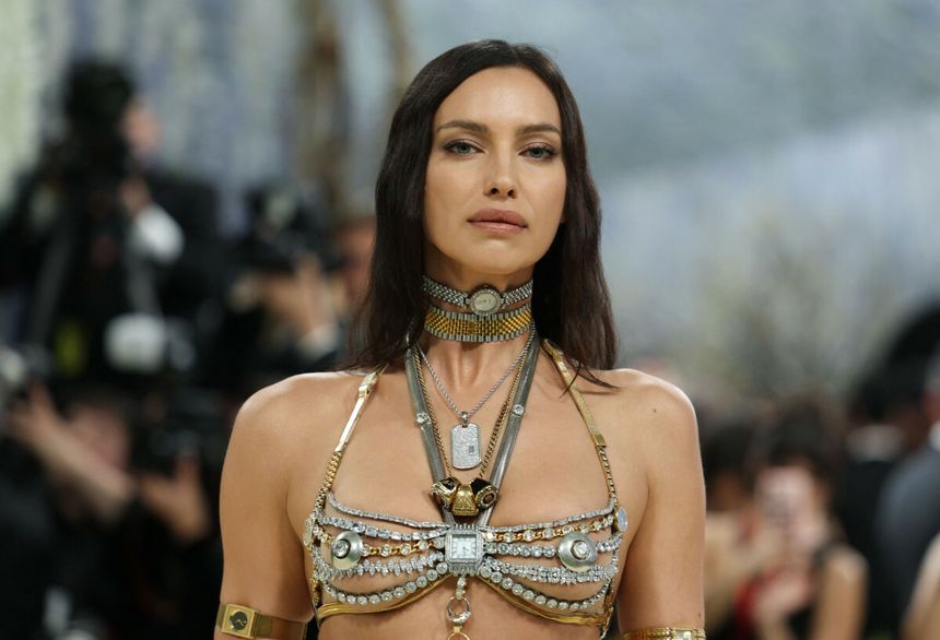 Irina Shayk w bogato zdobionej biżuterii, patrzy pewnie w obiektyw, otoczona przez paparazzi.