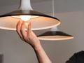 Osoba trzymając rękę pod lampą w kształcie klosza, podświetloną przez żarówkę.