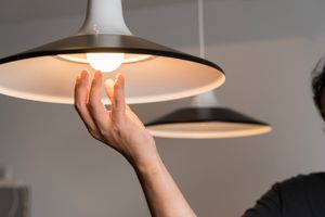 Osoba trzymając rękę pod lampą w kształcie klosza, podświetloną przez żarówkę.