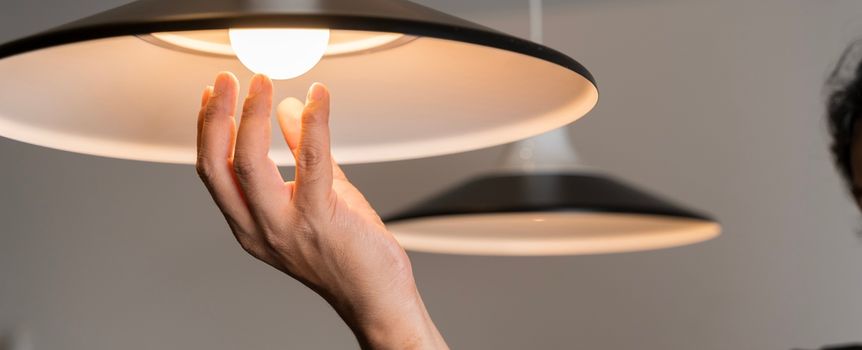 Osoba trzymając rękę pod lampą w kształcie klosza, podświetloną przez żarówkę.