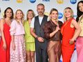 Grupa ośmiu osób w kolorowych strojach na tle logotypów telewizyjnych.