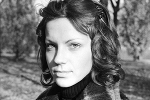 Młoda kobieta o kręconych włosach, w parku; szary, nostalgiczny klimat zdjęcia.