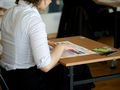 Kobieta w białej koszuli siedzi przy biurku z dokumentami i długopisami.