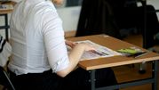 Kobieta w białej koszuli siedzi przy biurku z dokumentami i długopisami.