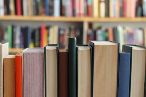 Zbliżenie na rząd zamkniętych książek w bibliotece, w tle nieczytelne powieści.