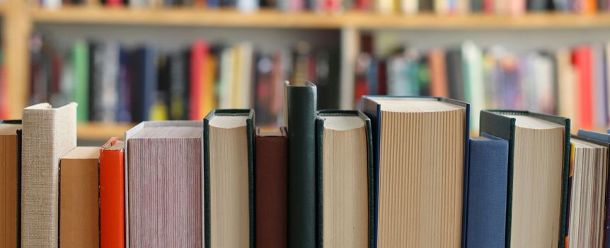 Zbliżenie na rząd zamkniętych książek w bibliotece, w tle nieczytelne powieści.