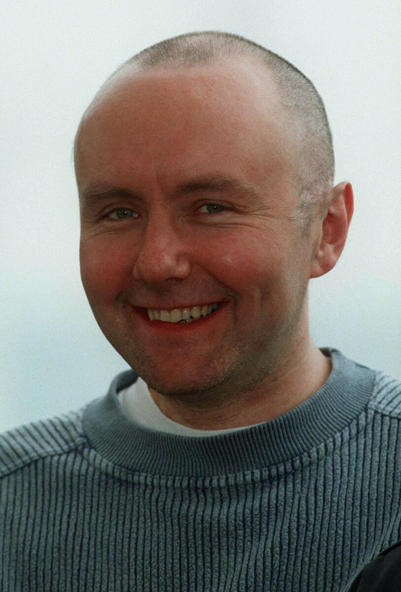 Mężczyzna z krótkimi włosami, uśmiecha się, ubrany w szary sweter.
