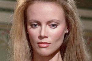 Kobieta o długich blond włosach, delikatnym makijażu, skupiona na czymś przed sobą.