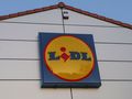 Logo sieci sklepów Lidl na ścianie budynku, w tle błękitne niebo.