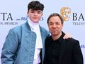Na zdjęciu dwóch mężczyzn uśmiecha się na tle banera BAFTA. Mężczyźni ubrani elegancko.