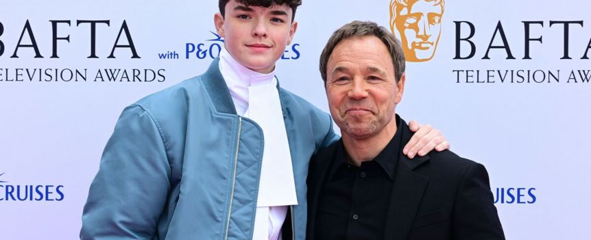Na zdjęciu dwóch mężczyzn uśmiecha się na tle banera BAFTA. Mężczyźni ubrani elegancko.