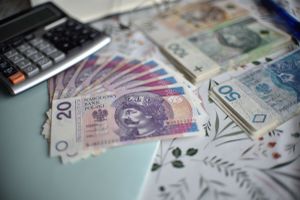 Na stole leżą banknoty w różnych nominałach obok kalkulatora i długopisu.