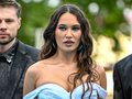 Trzy osoby w eleganckich strojach, z kobietą w jasnej sukience na pierwszym planie.