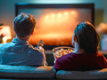 Para siedzi na sofie, oglądając telewizję. Kobieta trzyma miskę z popcornem.