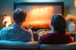Para siedzi na sofie, oglądając telewizję. Kobieta trzyma miskę z popcornem.