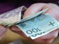 Osoba trzymająca banknoty, w tym sto złotych i pięćdziesiąt złotych.