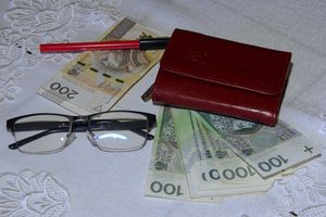 Na stole leżą okulary, portfel, długopis i banknoty w różnych nominałach.
