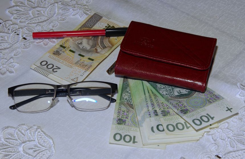 Na stole leżą okulary, portfel, długopis i banknoty w różnych nominałach.