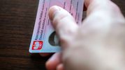 Na zdjęciu widoczna ręka trzymająca polski dowód osobisty na drewnianym stole.