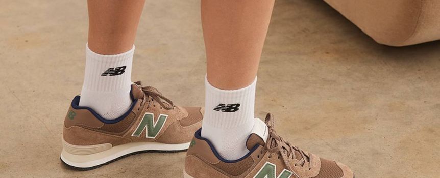 Para stóp w brązowych sneakersach New Balance na tle jasnej podłogi.