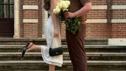 Młoda para na schodach, ona w białej sukience z czarnymi kropeczkami, on trzyma bukiet róż.
