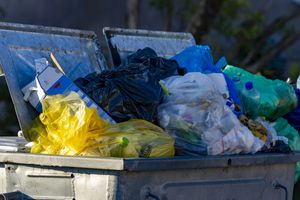 Złomowana śmietnik z różnokolorowymi workami na śmieci, pełen odpadków i zużytych opakowań.