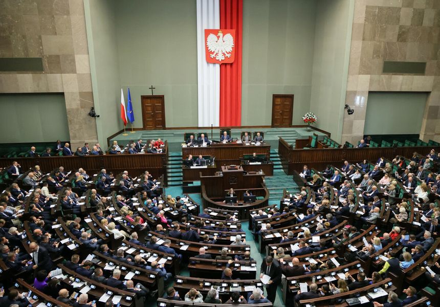 Zgromadzenie w Sejmie, z flagą Polski i orłem na ścianie, wielu przedstawicieli w sali.
